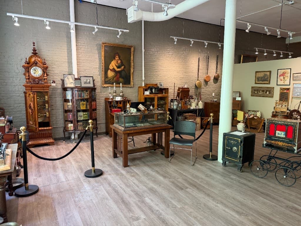Gallery corner containing an ornate clock, safes, cookware, sewing tools, cabinets, and a framed mother-and-child painting.